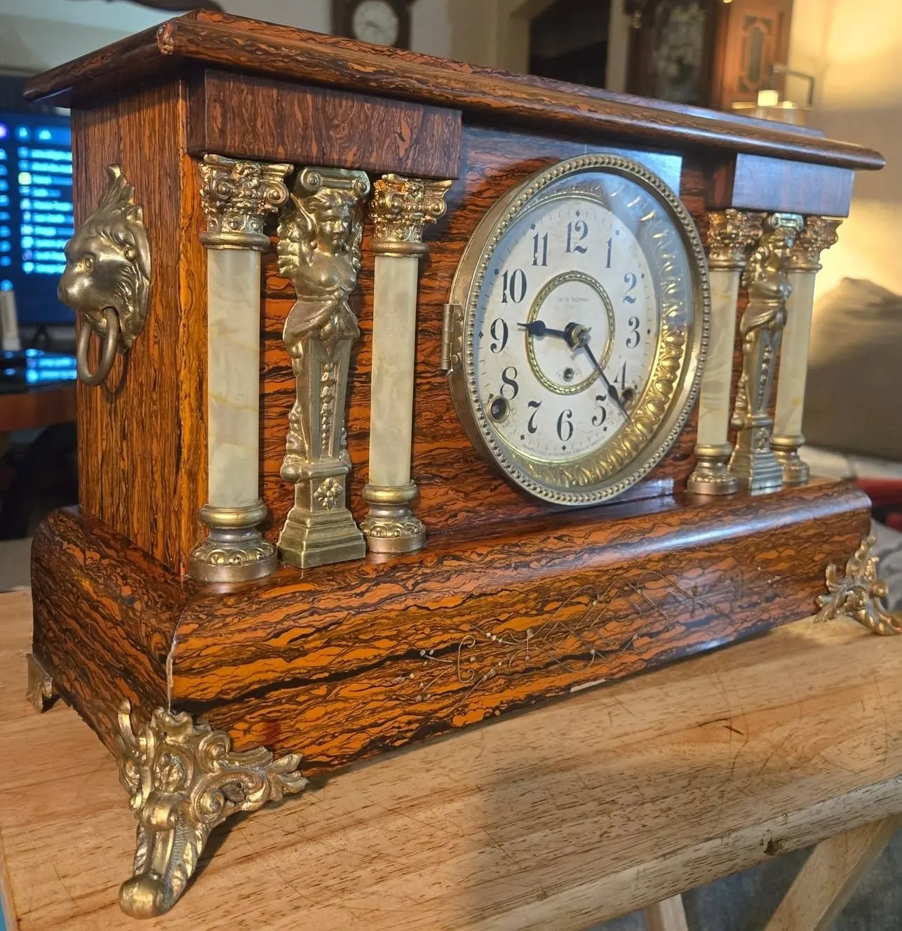 Ornate rosewood-grained mantel clock with figural cast-brass mounts, alabaster columns, and gilt Corinthian capitals