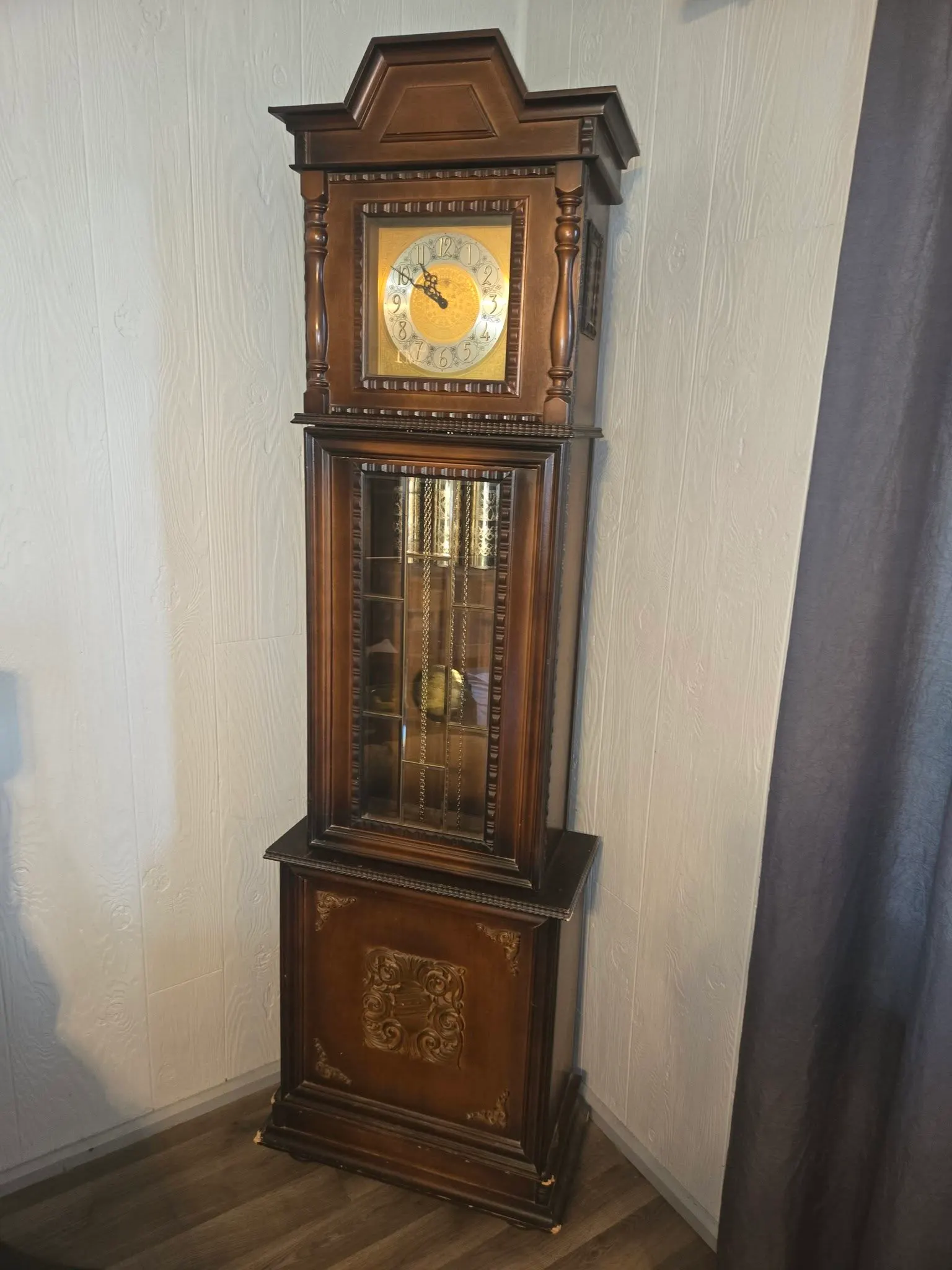 Full-height grandfather clock in medium-brown wood with brass dial and swinging pendulum